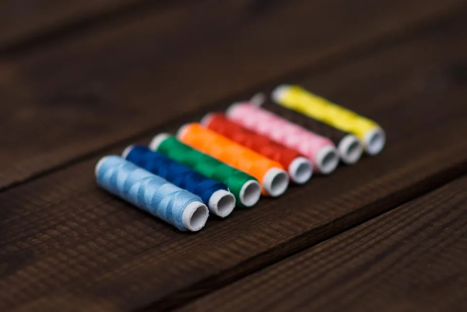 Row of coloured thread spools on a dark wooden table